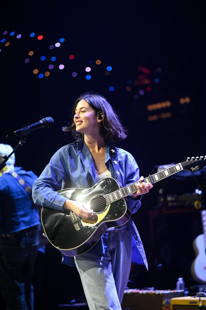 Gracie Abrams holds a guitar and smiles