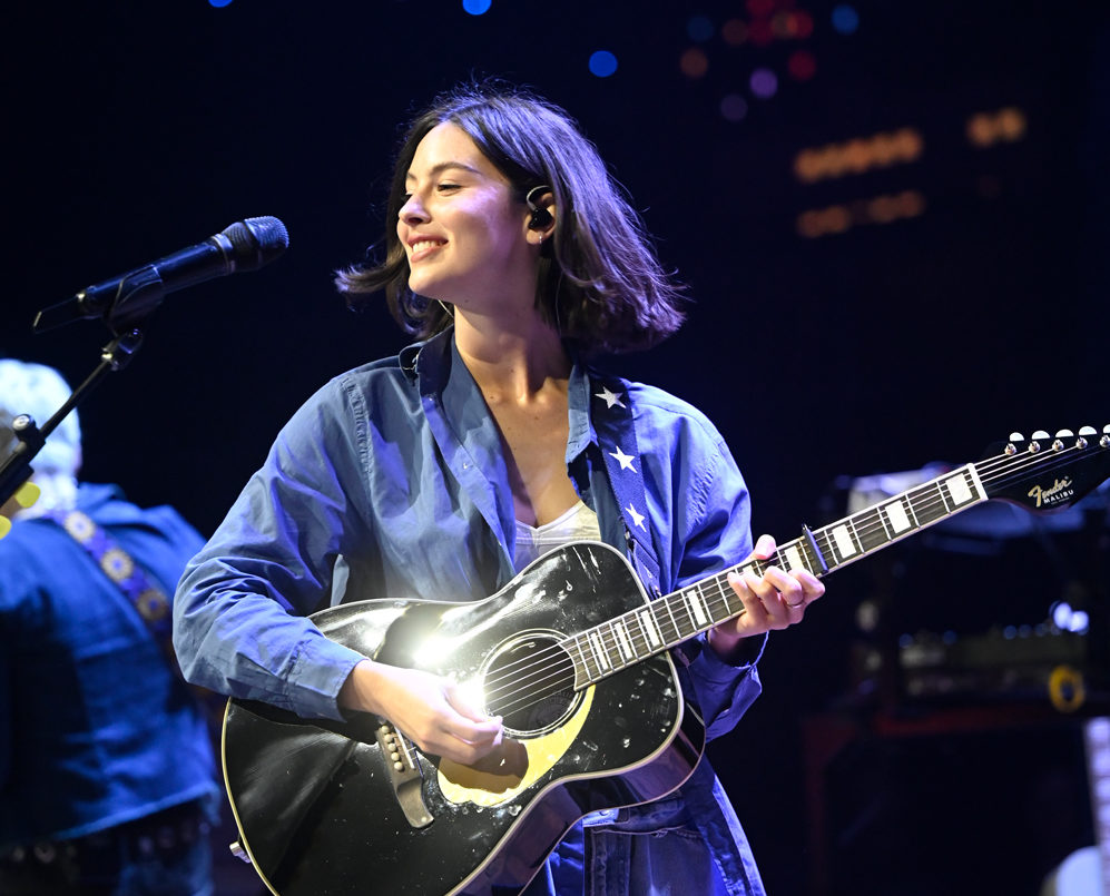 Gracie Abrams holds a guitar and smiles